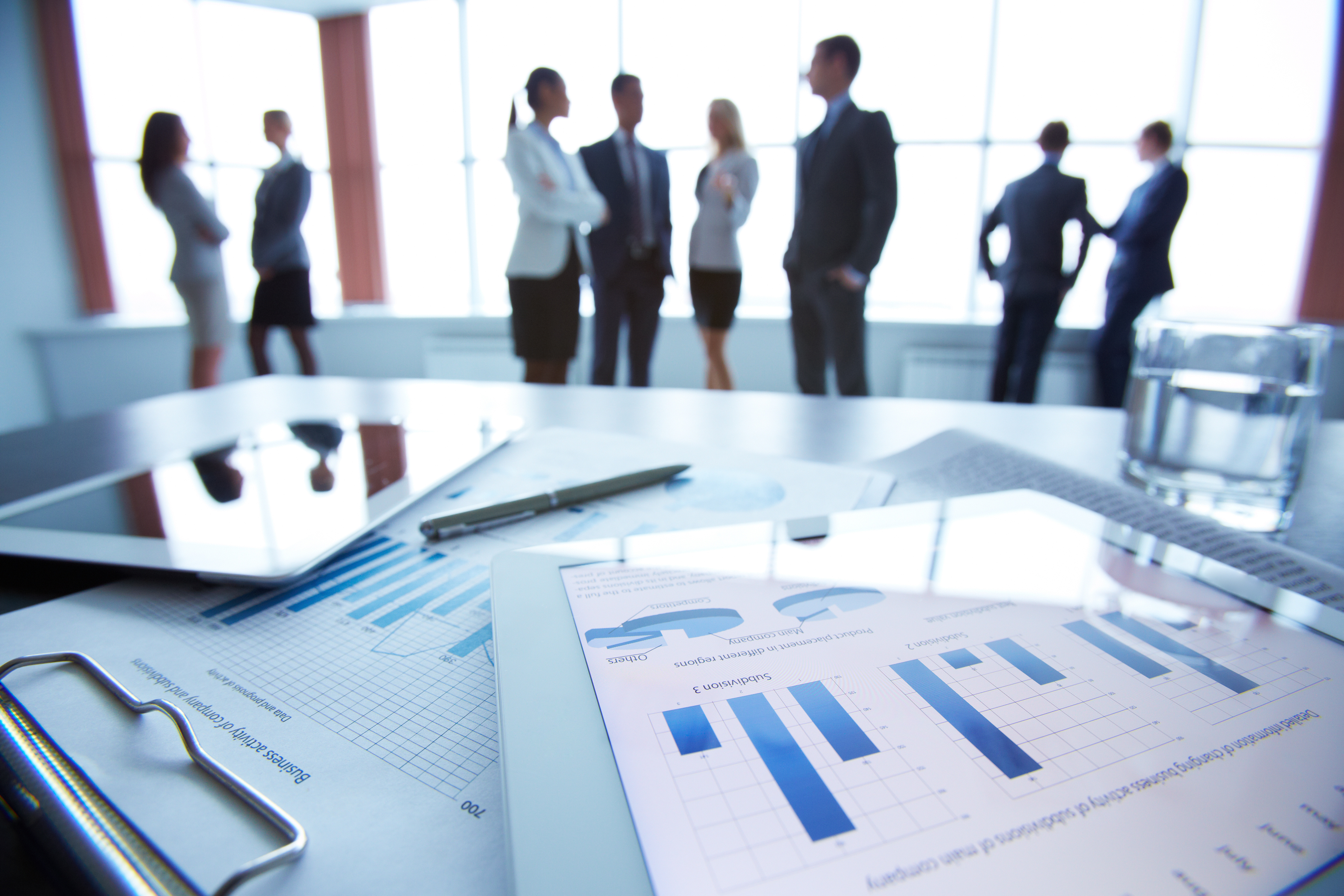 Close-up of business document in touchpad lying on the desk, office workers interacting in the background