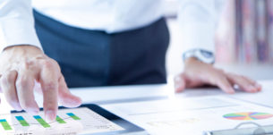 Business man touching a tablet touch screen analysing on business performance reports and returning on investment, ROI, or investment risk analysis.